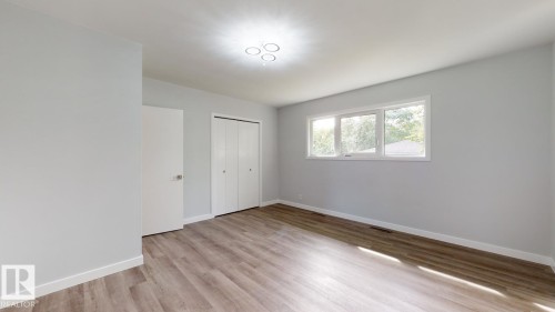 Spacious room featuring light gray walls, wood-finish flooring, a contemporary flush-mount light fixture, a large window, and double bi-fold closet doors - 11744 135 Street, Edmonton, AB - Indoor Photo Showing Other Room