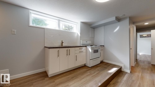 Compact kitchen area featuring white cabinetry, a white electric range, and a stainless steel faucet - 11744 135 Street, Edmonton, AB - Indoor Photo Showing Kitchen