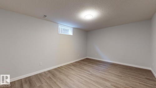Spacious room featuring light gray walls, wood-finish flooring, a white trim baseboard, and a ceiling-mounted flush light fixture - 11744 135 Street, Edmonton, AB - Indoor Photo Showing Other Room