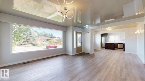 Spacious living area featuring light wood-finish flooring, a large picture window, a decorative entry door with glass inserts, and a modern ceiling light fixture - 11744 135 Street, Edmonton, AB - Indoor
