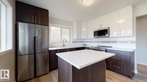 Modern kitchen featuring a white countertop island, stainless steel appliances, dark wood-finish lower cabinetry, white upper cabinetry, and wood-finish flooring - 11744 135 Street, Edmonton, AB - Indoor Photo Showing Kitchen With Stainless Steel Kitchen With Upgraded Kitchen