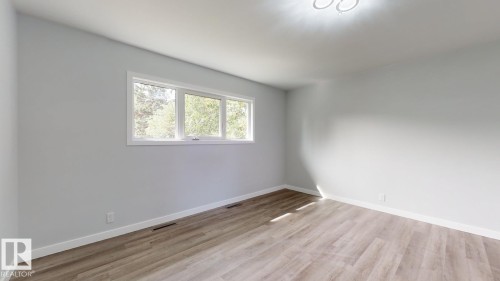 Spacious room featuring light-toned walls, wood-finish flooring, white baseboards, a three-panel window, and a flush-mount ceiling light fixture - 11744 135 Street, Edmonton, AB - Indoor Photo Showing Other Room