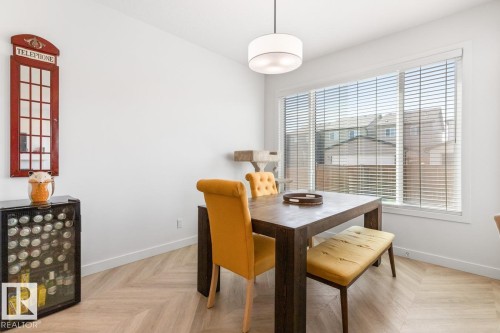 Spacious room featuring a large window with horizontal blinds, light wood-finish flooring in a herringbone pattern, a contemporary ceiling light fixture, and white painted walls - 117 Paisley Gate Gate, Edmonton, AB 