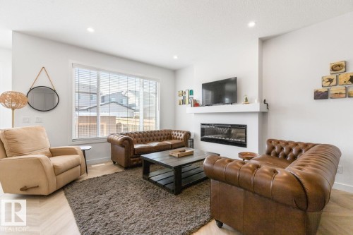 Living area featuring a sleek linear fireplace with a white mantel, large windows with blinds, and light wood-finish flooring - 117 Paisley Gate Gate, Edmonton, AB 
