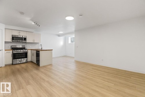 Open-concept living space featuring a kitchen with stainless steel appliances, white cabinetry, a tiled backsplash, and wood-finish flooring - 117 Paisley Gate Gate, Edmonton, AB 