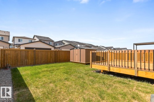 Expansive backyard featuring a natural wood deck with black metal balusters, a gravel border, lush green grass, a natural wood privacy fence, and a storage shed - 117 Paisley Gate Gate, Edmonton, AB 