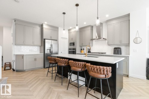 Contemporary kitchen featuring an oversized island with seating, light gray cabinetry, white subway tile backsplash, stainless steel appliances, and a gold-finish faucet - 117 Paisley Gate Gate, Edmonton, AB 