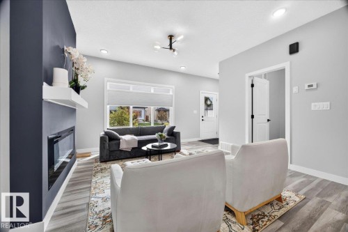 Living room featuring a contemporary electric fireplace with white floating mantel, wood-finish flooring, recessed lighting, and a front entry door with a frosted glass insert - 424 Black Stone Link, Leduc, AB 