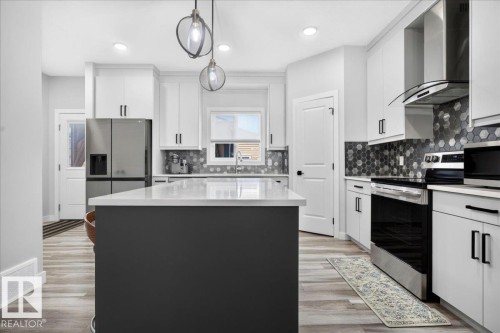 Modern kitchen featuring a central island with a white countertop, white cabinetry with black hardware, and wood-finish flooring - 424 Black Stone Link, Leduc, AB 