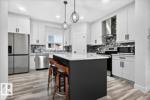 Modern kitchen featuring white cabinetry, a dark-toned island with a white countertop, and wood-finish flooring - 424 Black Stone Link, Leduc, AB 