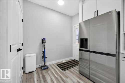 Kitchen area featuring a stainless steel refrigerator with an external ice and water dispenser, white cabinetry with black hardware, wood-finish flooring, and a white paneled door - 424 Black Stone Link, Leduc, AB 