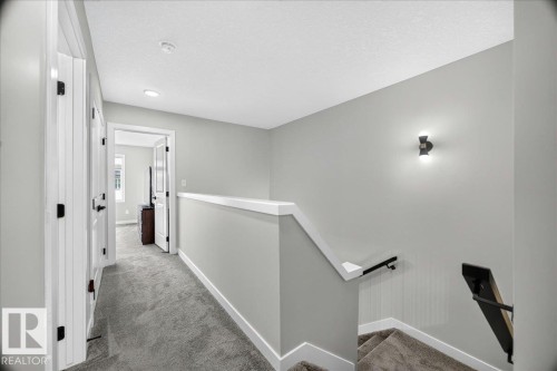 Upper-level hallway featuring plush gray carpeting, white trim, and a contemporary wall sconce - 424 Black Stone Link, Leduc, AB 