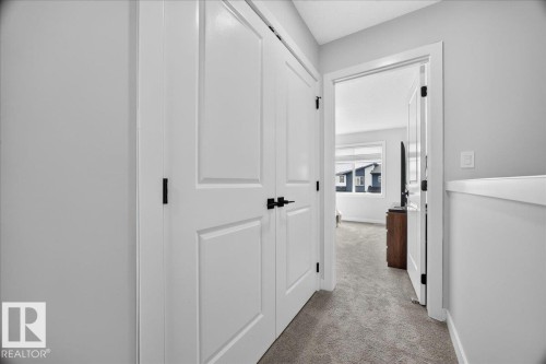 Hallway featuring light gray carpeting, white painted walls, and white paneled doors with black hardware - 424 Black Stone Link, Leduc, AB 