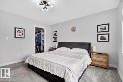 Carpeted bedroom featuring a black upholstered bed frame, a walk-in closet with built-in shelving, a modern sputnik-style ceiling light fixture, and a window providing natural light - 424 Black Stone Link, Leduc, AB 
