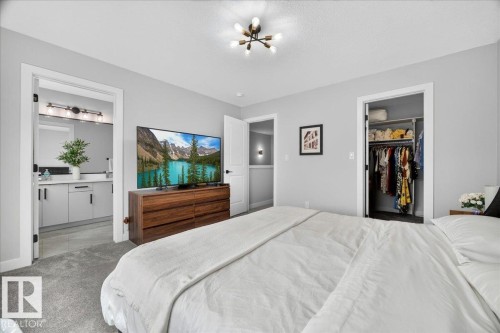 Carpeted room featuring a ceiling-mounted sputnik light fixture, a door opening to a bathroom with a modern vanity and wall-mounted light bar, another door opening to a closet with built-in shelving, and light gray walls - 424 Black Stone Link, Leduc, AB 
