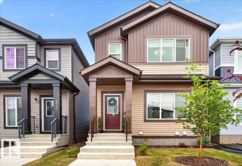 Two-story residence featuring a multi-toned exterior with horizontal siding and vertical paneling, a covered front entry with a dark red door, white-framed windows, and a concrete staircase with black handrails - 424 Black Stone Link, Leduc, AB 