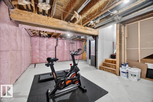 Unfinished basement space featuring exposed wooden joists, insulated exterior walls, concrete flooring, and a wooden staircase - 424 Black Stone Link, Leduc, AB 