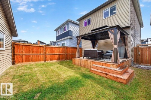 Expansive backyard featuring a manicured lawn, full wood privacy fencing, and a multi-level wood deck with integrated steps - 424 Black Stone Link, Leduc, AB 