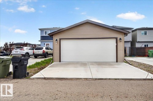 Detached garage with tan siding, a white overhead door, and two exterior sconce lights - 424 Black Stone Link, Leduc, AB 