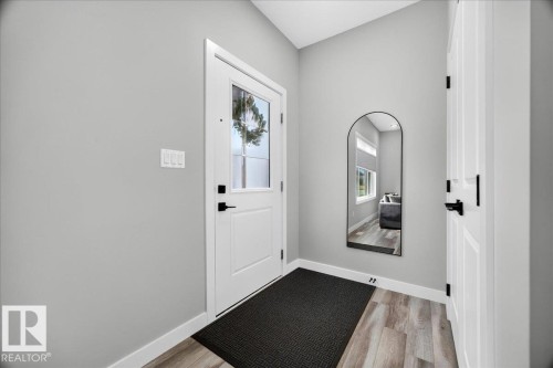 Entryway featuring a white paneled door with glass inserts and matte black hardware, wood-finish flooring, light gray wall tones, and white baseboards - 424 Black Stone Link, Leduc, AB 