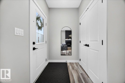 Entryway featuring a white paneled door with a clear glass insert, matte black hardware, and wood-finish flooring - 424 Black Stone Link, Leduc, AB 