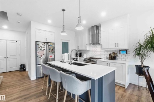 Modern kitchen featuring white shaker cabinetry, stainless steel appliances, a subway tile backsplash, and a central island with a white countertop and seating - 9323 223 Street, Edmonton, AB 