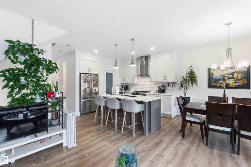 Open-concept living space featuring wood-finish flooring, a contemporary kitchen island with seating, stainless steel appliances, white subway tile backsplash, and a dedicated dining area with an overhead chandelier - 9323 223 Street, Edmonton, AB 