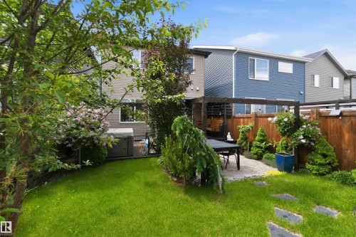 Private backyard featuring a stone patio with pergola, surrounded by mature trees, shrubs, and a wooden fence - 9323 223 Street, Edmonton, AB 