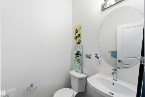 Powder room with a white toilet, wall-mounted sink, oval mirror, and chrome faucet - 9323 223 Street, Edmonton, AB 