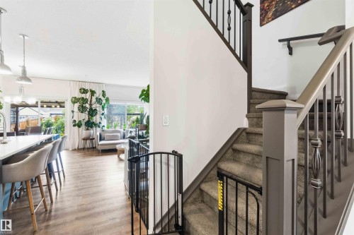 Open-concept living space featuring wood-finish flooring, a kitchen island with seating, pendant lighting, and abundant natural light from large windows - 9323 223 Street, Edmonton, AB 