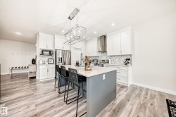 Modern kitchen featuring a central island with a light-toned countertop and contrasting base, white shaker-style cabinetry, and wood-finish flooring - 