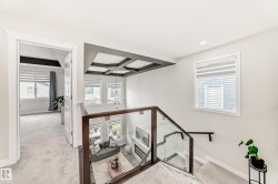 Upper-level landing featuring a glass railing, coffered ceiling detail, and carpeted flooring - 