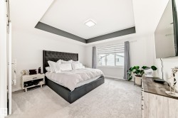 Spacious bedroom featuring plush carpeting, a large window with horizontal blinds and drapery, a tray ceiling with a dark accent, and a built-in ceiling light fixture - 