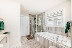 Bathroom featuring a large soaker tub, glass-enclosed shower, wall-mounted vanity with integrated sink, wood-finish tile flooring, and a large window with privacy blinds - 