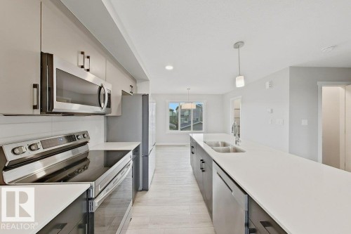 Contemporary kitchen featuring an expansive island with an undermount double sink, stainless steel appliances, light-toned cabinetry, and wood-finish flooring - 5034 Rivers Edge Way, Edmonton, AB 