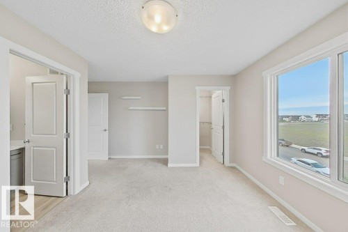 Carpeted room with a large window, providing natural light - 5034 Rivers Edge Way, Edmonton, AB 