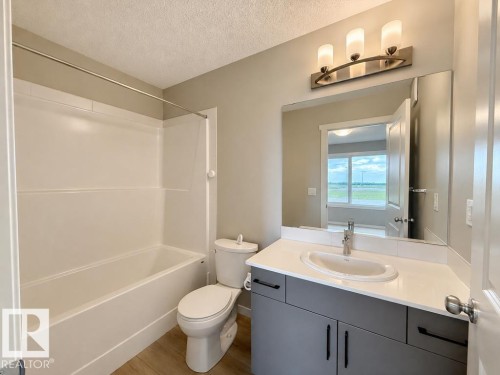 Modern bathroom featuring a white bathtub and shower surround, a sleek vanity with a solid surface countertop, an undermount sink, and wood-finish flooring - 5034 Rivers Edge Way, Edmonton, AB 