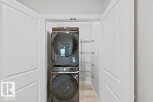 Dedicated laundry closet featuring a stackable washer and dryer, light wood-finish flooring, and integrated wire shelving for storage - 5034 Rivers Edge Way, Edmonton, AB 