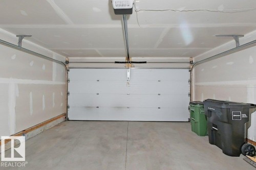 Attached garage featuring a white sectional door, concrete flooring, and an automatic garage door opener - 5034 Rivers Edge Way, Edmonton, AB 