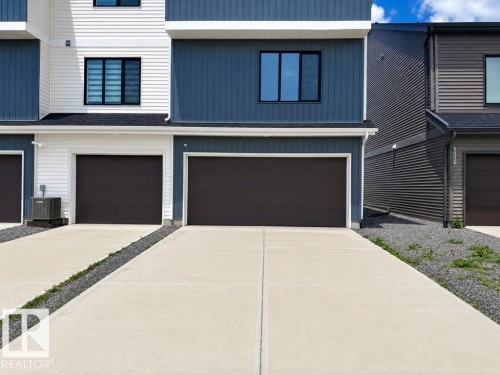 Contemporary multi-level facade featuring blue and white horizontal siding, black-framed windows, and a dark garage door - 5034 Rivers Edge Way, Edmonton, AB 