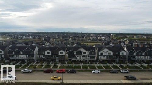Modern residential streetscape featuring multi-level townhomes with dark siding, white trim, and individual front walkways - 5034 Rivers Edge Way, Edmonton, AB 