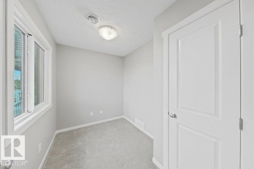 Carpeted room featuring a double-paned window, neutral wall paint, white trim, and a paneled door - 5034 Rivers Edge Way, Edmonton, AB 