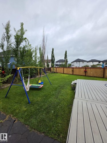 Expansive green lawn featuring a composite deck with integrated lighting, a natural wood privacy fence, and mature trees - 13 Baie Madelene, Beaumont, AB 