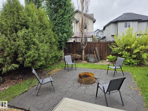 Private backyard featuring a stamped concrete patio, a built-in fire pit, mature evergreen trees, and a wooden privacy fence - 13 Baie Madelene, Beaumont, AB 