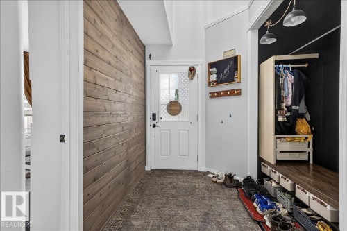 Entryway featuring a decorative accent wall, a white entry door with a frosted glass insert, and patterned flooring - 13 Baie Madelene, Beaumont, AB 
