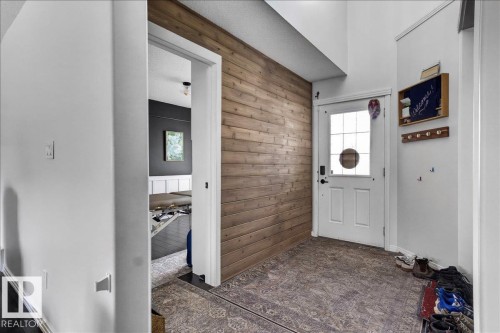 Foyer featuring a wood-panel accent wall, white entry door with a multi-pane glass insert, and patterned flooring - 13 Baie Madelene, Beaumont, AB 
