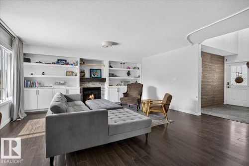 Living room featuring wood-finish flooring and a fireplace with a stone surround - 13 Baie Madelene, Beaumont, AB 