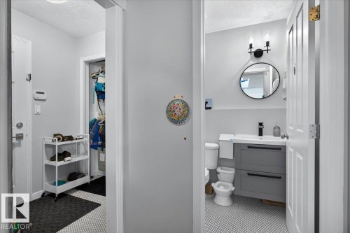 Bathroom featuring a wall-mounted vanity with a white rectangular sink, dark gray cabinetry with black hardware, and a black circular mirror - 13 Baie Madelene, Beaumont, AB 