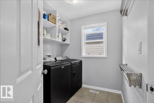 Dedicated laundry room featuring ceramic tile flooring, built-in shelving, and a wall-mounted drying rack - 13 Baie Madelene, Beaumont, AB 