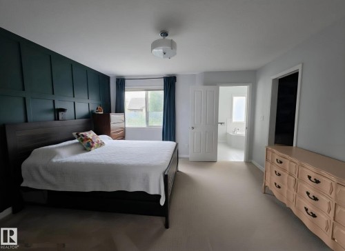 Bedroom featuring a dark accent wall with panel detailing, light-toned carpeting, and a window with dark drapery - 13 Baie Madelene, Beaumont, AB 